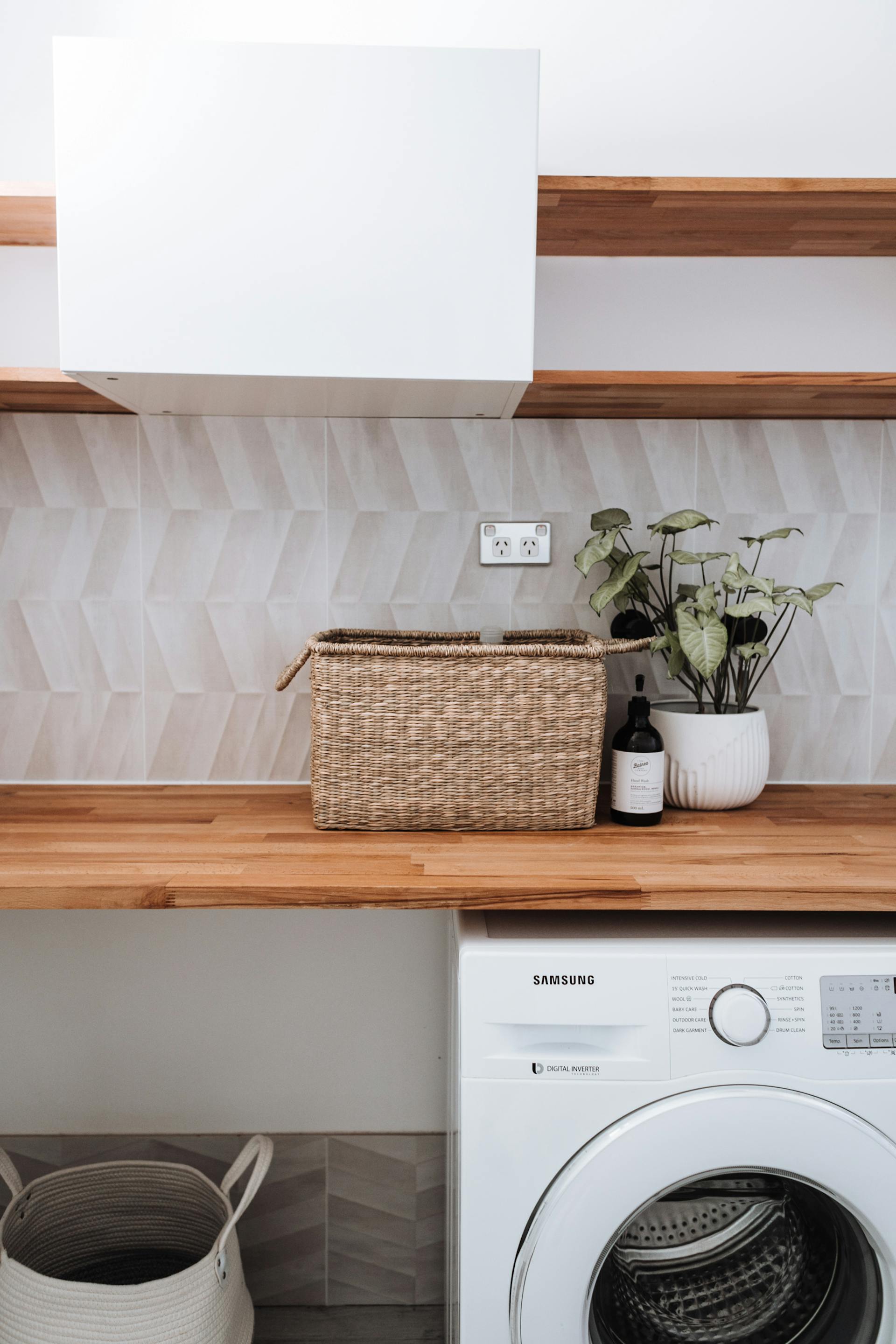 A washing machine under a wooden table with a plant and a wicker basket | Source: Pexels