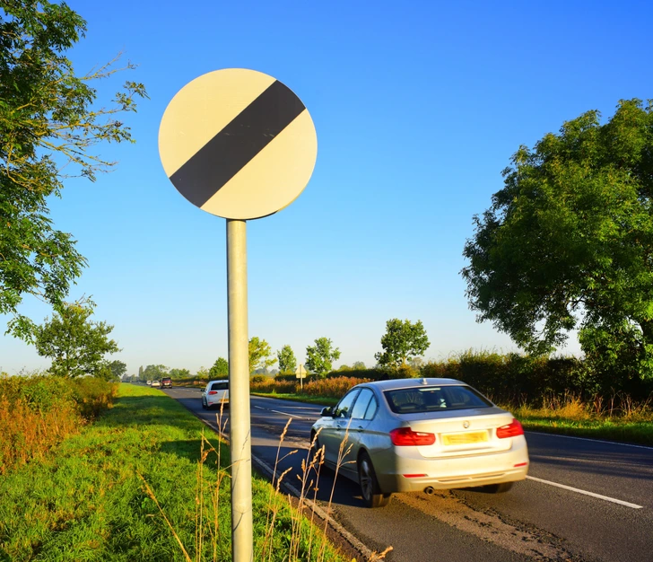 “The white circular sign with a black diagonal stripe indicates the national speed limit on the upcoming road stretch, overriding any previous speed limit signs”