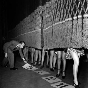 A curtain, a lineup of beautiful legs, and curious eyes eagerly waiting…What on earth is happening here? Can you guess?